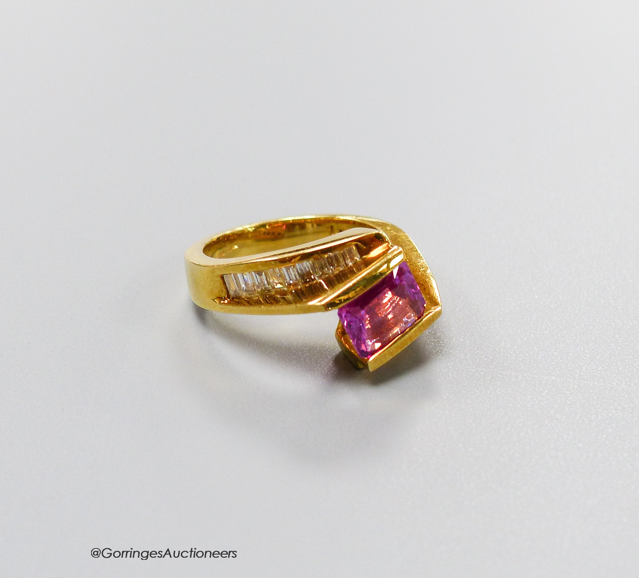 A modern 18k gold, emerald cut pink sapphire set dress ring, with graduated baguette cut diamond set shoulders, size M, gross weight 8.6 grams.